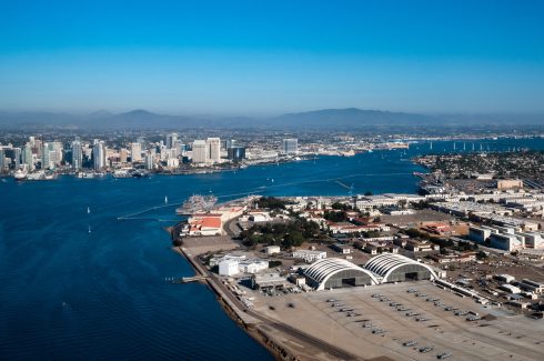 Aerial view of North Island Naval Air Base on Coronado and downtown San Diego California while flying over the bay with boats on the water and mountains in the background during daylight